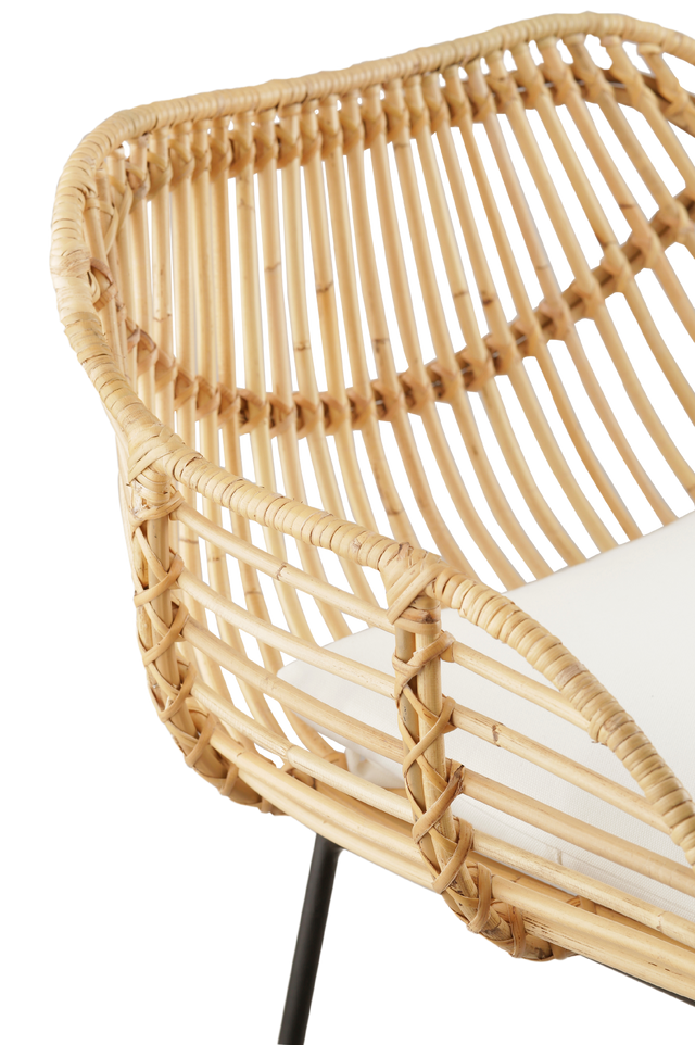 Close up on materials. modern counter stool with a rattan seat and backrest, featuring a unique, curved design. The stool has a comfortable white cushioned seat and is supported by slim black metal legs, creating a contrast with the natural rattan. Its contemporary design makes it an ideal choice for stylish, relaxed interiors.