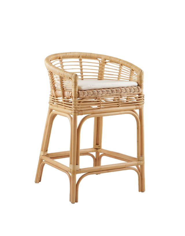 comfortable counter stool made from rattan, featuring a woven seat and backrest with armrests. The stool has a cushioned seat for added comfort and a natural rattan frame with intricate weaving. Its relaxed yet stylish design makes it a perfect fit for modern or coastal-inspired interiors. 3/4 view of the stool